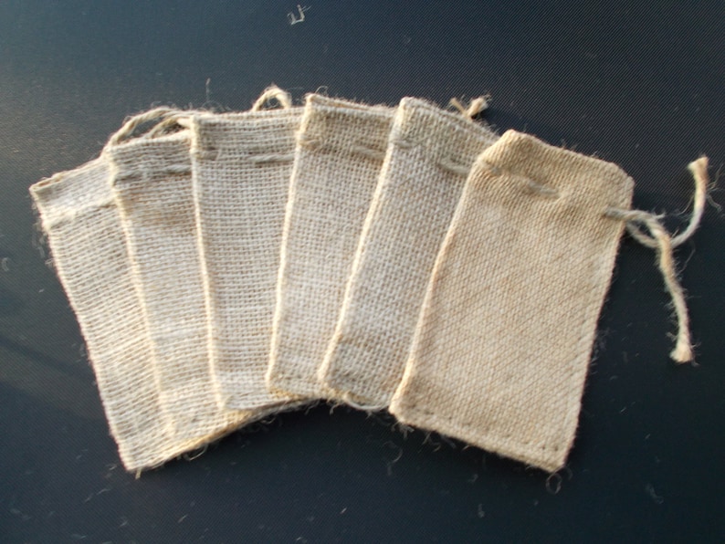 Op de afbeelding: Zes kleine, rechthoekige jute zakjes met trekkoord zijn in een waaier gerangschikt. De zakjes hebben een natuurlijke, bruinachtige kleur met een zichtbare geweven textuur. Elk zakje heeft een trekkoordsluiting aan de bovenkant.