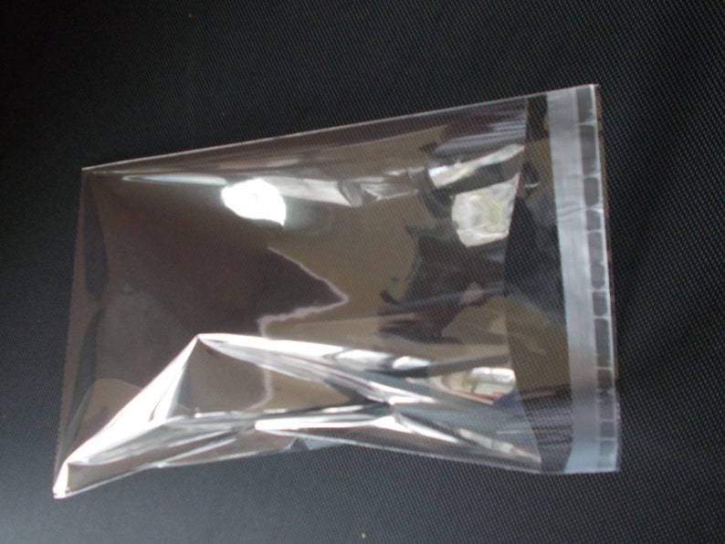 May include: A clear, rectangular cellophane bag with a self-sealing adhesive strip. The bag is transparent, allowing visibility of the contents. The bag is designed for packaging and protecting items.