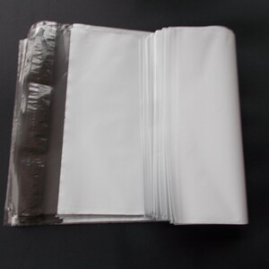 May include: A stack of white, folded paper sheets, partially wrapped in clear plastic. The paper is bright white, and the plastic wrap is transparent, revealing the paper's edges. The background is a solid black.