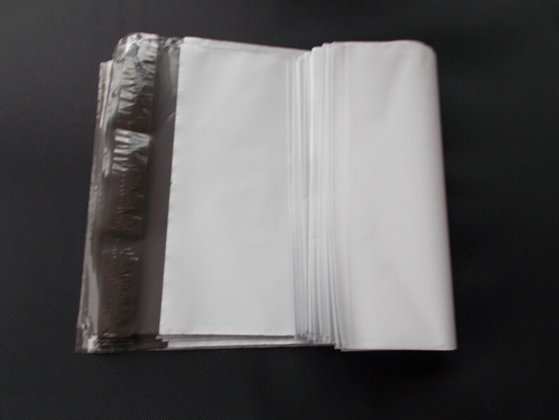May include: A stack of white, folded paper sheets, partially wrapped in clear plastic. The paper is bright white, and the plastic wrap is transparent, revealing the paper's edges. The background is a solid black.