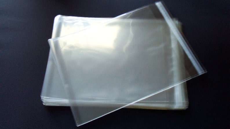 May include: A stack of clear, transparent plastic sleeves. The sleeves are rectangular and appear to be sealed on three sides, with the fourth side open. The plastic is smooth and reflects light, creating highlights and shadows.