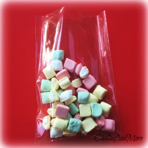 May include: A clear plastic bag filled with colorful, square-shaped marshmallows. The marshmallows are pastel shades of pink, yellow, green, and white. The bag is on a red background. The text "ChellosAndMore" is in the bottom right corner.