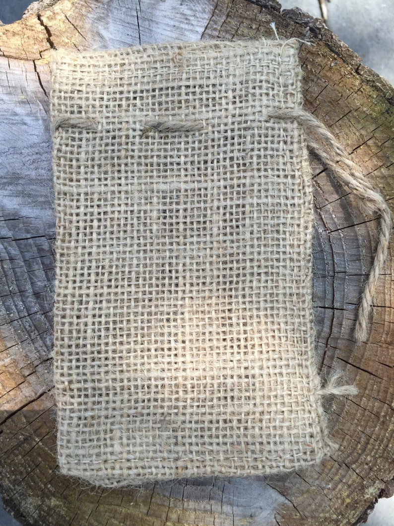 K&ouml;nnte beinhalten: Ein rechteckiger Jutebeutel mit Kordelzug. Die Tasche besteht aus einem groben, gewebten Stoff in Naturfarbe. Ein St&uuml;ck Schnur wird als Kordelzug verwendet. Die Tasche liegt auf einer Holzoberfl&auml;che.