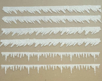 May include: White, glittery, decorative icicle trim in varying lengths. The trim has a jagged edge, resembling icicles. The image shows six strips of the trim, perfect for winter or holiday crafts and decorations.