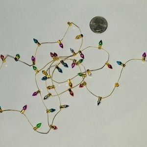 May include: A string of miniature Christmas lights with multi-colored bulbs. The lights are strung on a gold wire and are about the size of a US quarter.
