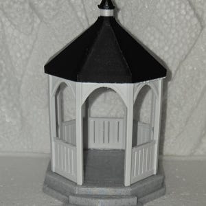 Könnte beinhalten: Ein Miniatur-Pavillon-Modell mit schwarzem Dach und weißen Wänden. Der Pavillon hat eine achteckige Form mit gewölbten Öffnungen und einem kleinen Geländer. Der Sockel ist grau mit Stufen, die zum Pavillon führen.