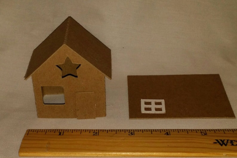 Puede incluir: Una peque&ntilde;a casa de cart&oacute;n sin terminar con un recorte en forma de estrella y una pieza de techo separada con una ventana. Una regla de madera se coloca junto a la casa. La casa mide aproximadamente 7,6 cm de altura.