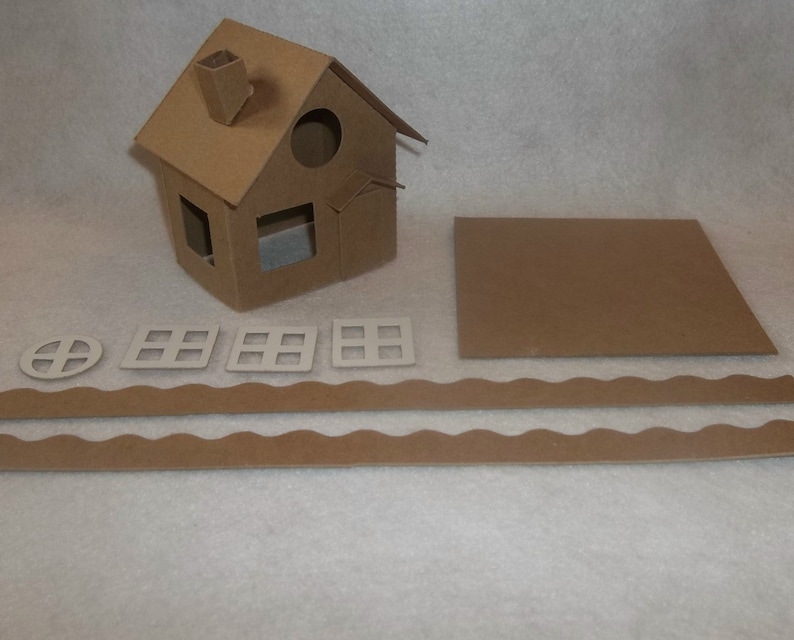 May include: A DIY cardboard house kit with a pitched roof, chimney, and window cutouts. Includes separate pieces for windows, a base, and decorative trim. The house is made of brown corrugated cardboard.