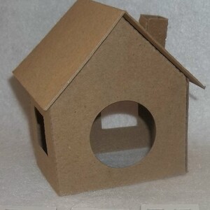 May include: A small, brown cardboard house with a pitched roof, chimney, and a circular opening. The house has a rectangular window and is constructed from a single piece of cardboard. The overall design is simple and minimalist.