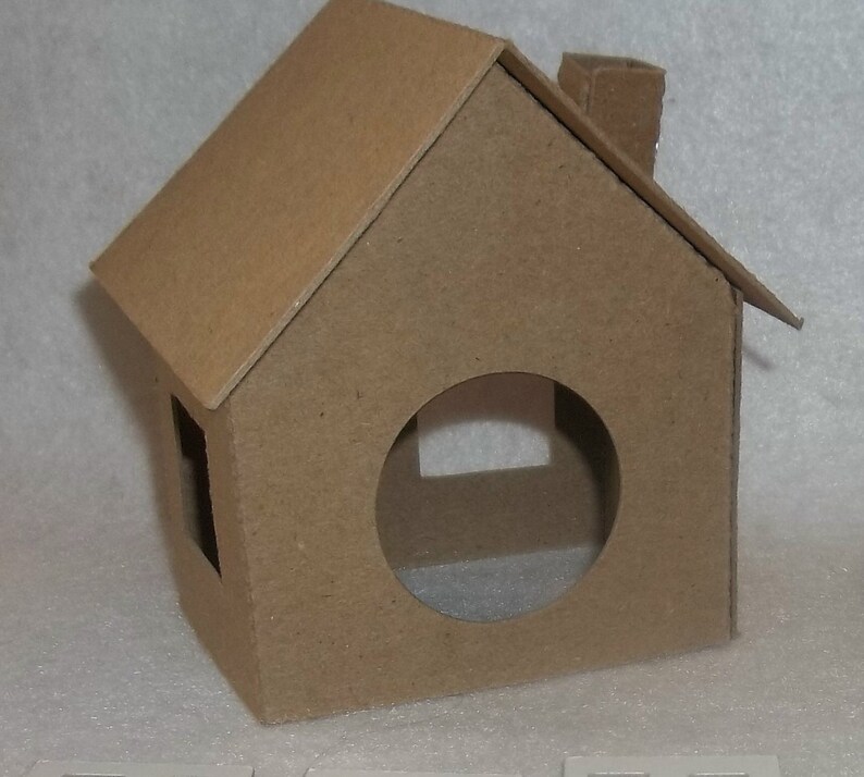 May include: A small, brown cardboard house with a pitched roof, chimney, and a circular opening. The house has a rectangular window and is constructed from a single piece of cardboard. The overall design is simple and minimalist.