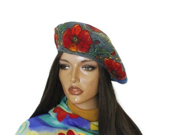 May include: A gray wool beret adorned with vibrant red poppy flower designs. The beret features detailed floral embroidery with green stems and leaves. The hat has a blue trim and is set against a white background.