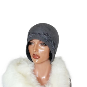 May include: A gray felt cloche hat with a black embroidered floral design around the brim.
