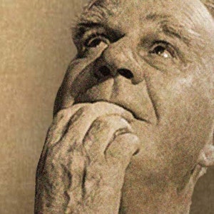 May include: Sepia-toned portrait of an older person, looking upwards with a contemplative expression. The person's hand is raised to their face, with fingers touching their mouth. The image is a close-up, focusing on the face and hand.