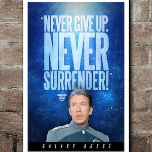 May include: A poster with the text "NEVER GIVE UP. NEVER SURRENDER!" in large, light blue letters against a dark blue, starry background. The poster features an image of an actor in a uniform and the words "GALAXY QUEST" at the bottom.