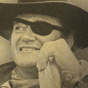 May include: Sepia-toned portrait of a man wearing a cowboy hat and an eye patch. The man is smiling, with his hand resting on his chin. The image has a vintage, weathered appearance.