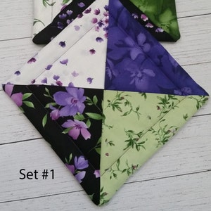 Puede incluir: Conjunto de dos agarraderas acolchadas con un dise&ntilde;o de patchwork que presenta telas florales y a rayas en tonos de morado, verde y blanco. El texto "Set #1" es visible en la esquina inferior izquierda de la imagen.