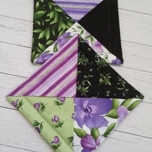 Puede incluir: Conjunto de dos agarraderas de olla de tela p&uacute;rpura, verde y negra con un patr&oacute;n floral. Las agarraderas tienen forma de diamante y est&aacute;n apiladas una encima de la otra. El texto "Set #4" es visible en la esquina inferior izquierda de la imagen.