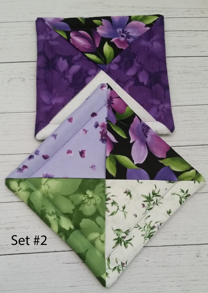 Puede incluir: Conjunto de dos posavasos de tela floral de color morado, verde y blanco. Los posavasos son cuadrados y tienen un dise&ntilde;o acolchado. El texto "Set #2" es visible en la esquina inferior izquierda de la imagen.