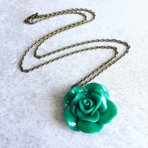 Puede incluir: Un collar con un colgante de rosa verde en una cadena de bronce. La rosa est&aacute; hecha de arcilla polim&eacute;rica y tiene un acabado brillante.