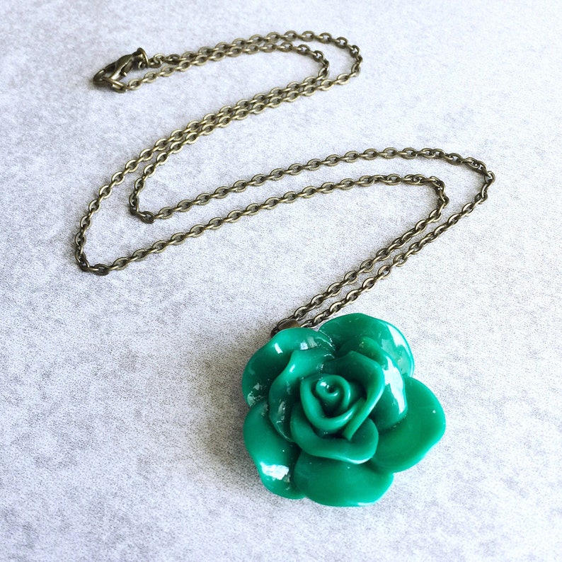 Puede incluir: Un collar con un colgante de rosa verde en una cadena de bronce. La rosa est&aacute; hecha de arcilla polim&eacute;rica y tiene un acabado brillante.