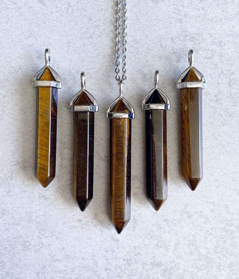 May include: Five gold tiger's eye crystal point pendants with silver caps. The pendants are arranged in a row, with the top pendant hanging from a silver chain.