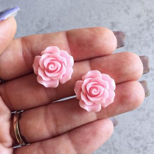 Peut inclure: Deux cabochons en r&eacute;sine de forme rose de couleur rose. Les cabochons mesurent environ 2,5 cm de diam&egrave;tre et pr&eacute;sentent un design en relief tridimensionnel.
