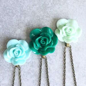 Puede incluir: Tres colgantes con forma de rosa en cadenas delicadas. Las rosas est&aacute;n hechas de un material liso y brillante y vienen en tonos de azul claro, turquesa y verde.