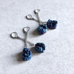 May include: Three pairs of earrings with blue and purple iridescent crystal druzy stones hanging from silver chains.