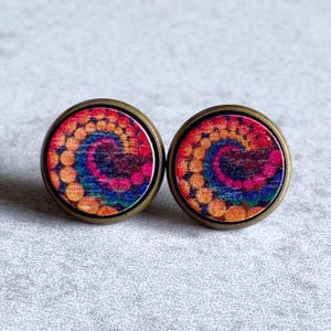 May include: A pair of round stud earrings with a colorful tie-dye design. The earrings feature a spiral pattern in shades of red, orange, yellow, blue, and purple. The earrings have a bronze-colored metal border and are set against a neutral background.