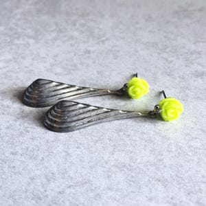 May include: A pair of silver earrings with a long, curved, and ridged design. Each earring is topped with a bright yellow rose-shaped charm.