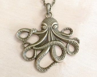 Op de afbeelding: Een bronzen octopus hanger ketting. De octopus heeft gedetailleerde tentakels met zuignappen en een getextureerde kop. De ketting is ook bronskleurig. Een sieraad met een nautisch thema.