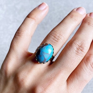 May include: A ring with a blue and brown oval stone set in a gold-toned bezel with a decorative edge.