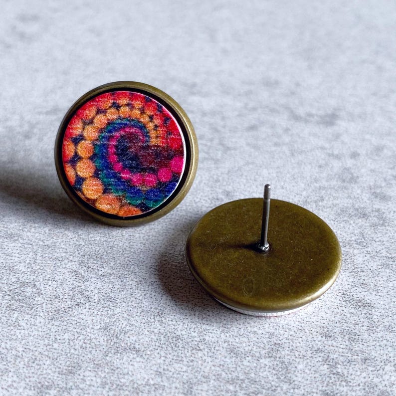May include: A pair of round stud earrings with a tie-dye design. The earrings feature a colorful spiral pattern in shades of orange, pink, blue, and green. The earrings have a bronze-colored metal setting and post.