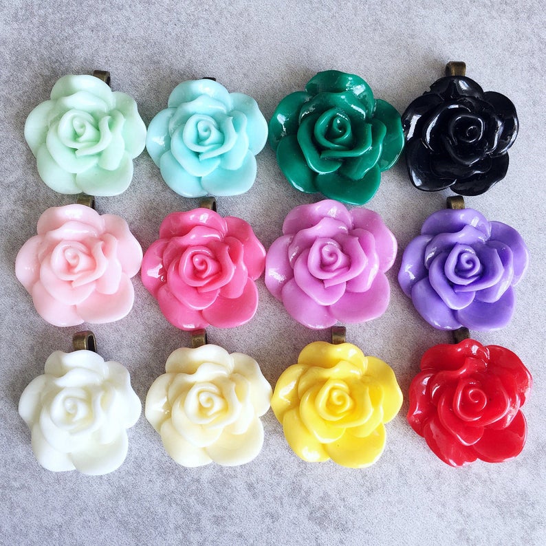 May include: Twelve different colored resin rose flower charms with a silver loop for hanging. The colors include pink, light pink, light blue, green, black, white, yellow, red, and purple.