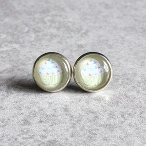 May include: A pair of silver stud earrings with a cupcake design. The cupcakes are light blue with white frosting and colorful sprinkles.