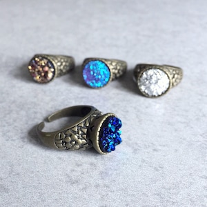 Peut inclure: Quatre bagues avec des pierres de cristal de diff&eacute;rentes couleurs. Les bagues sont en laiton et ont un design d&eacute;taill&eacute;. Les pierres sont bleues, blanches, violettes et brunes.