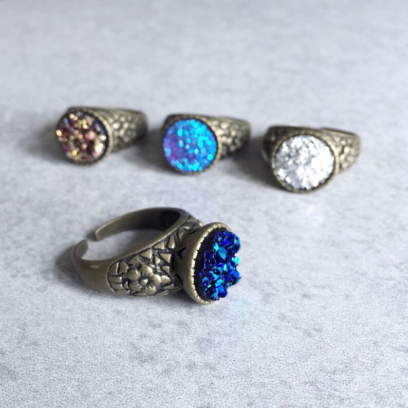 Peut inclure: Quatre bagues avec des pierres de cristal de diff&eacute;rentes couleurs. Les bagues sont en laiton et ont un design d&eacute;taill&eacute;. Les pierres sont bleues, blanches, violettes et brunes.