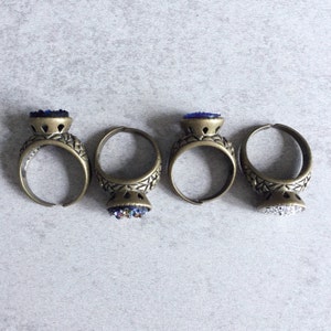 Peut inclure: Trois bagues en or avec des pierres en verre bleu et blanc. Les bagues ont un design en filigrane et sont pos&eacute;es sur un fond gris.