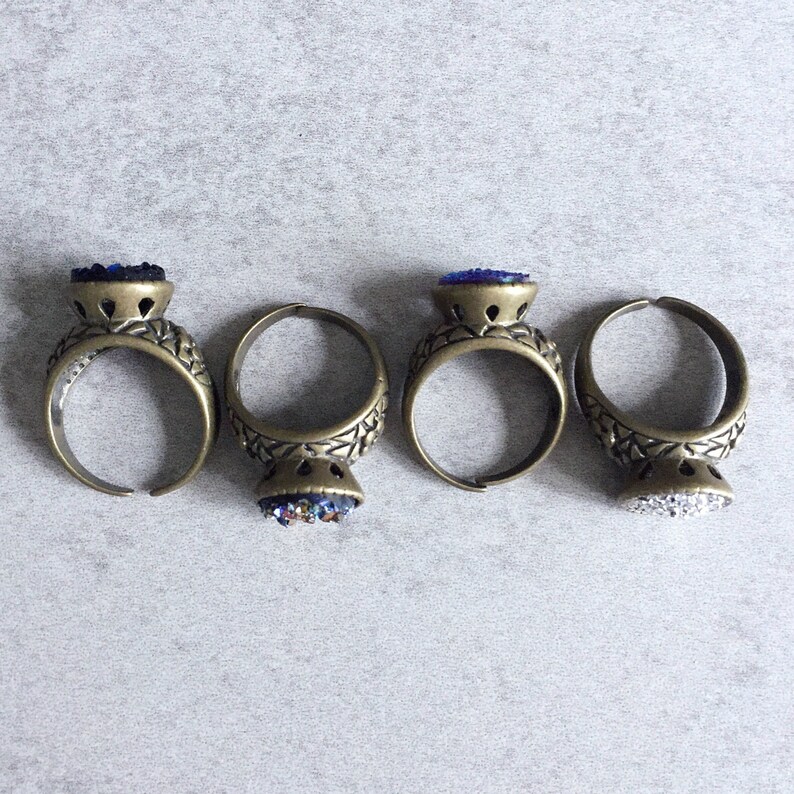 Peut inclure: Trois bagues en or avec des pierres en verre bleu et blanc. Les bagues ont un design en filigrane et sont pos&eacute;es sur un fond gris.