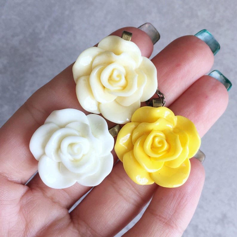 May include: Three resin rose flower charms in white and yellow. The charms are attached to a metal loop for hanging.