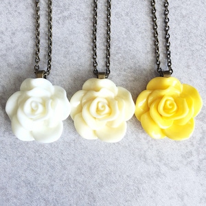 May include: Three necklaces with rose-shaped pendants. The roses are made of white and yellow resin. The chains are bronze.