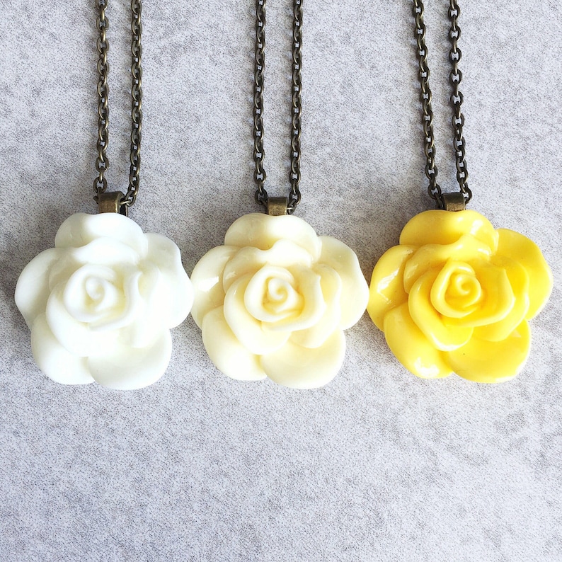May include: Three necklaces with rose-shaped pendants. The roses are made of white and yellow resin. The chains are bronze.
