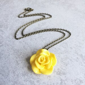 May include: A yellow rose pendant necklace with a bronze chain. The rose is made of polymer clay and has a realistic look.