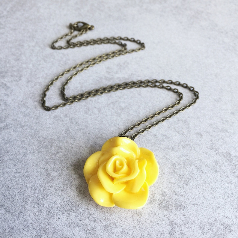 May include: A yellow rose pendant necklace with a bronze chain. The rose is made of polymer clay and has a realistic look.