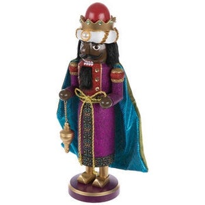 May include: A decorative wooden nutcracker figurine of a king, featuring a black face, a red crown, and a white and gold turban. The king wears a purple and gold coat with a teal cape and holds a gold pendulum. The figurine stands on a purple base.