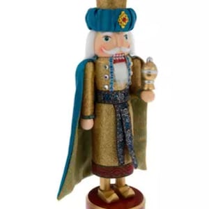 May include: A decorative wooden nutcracker figurine. The nutcracker is dressed in a gold and teal outfit with a matching hat. It has a white mustache and holds a golden scepter. The base is a dark red color.