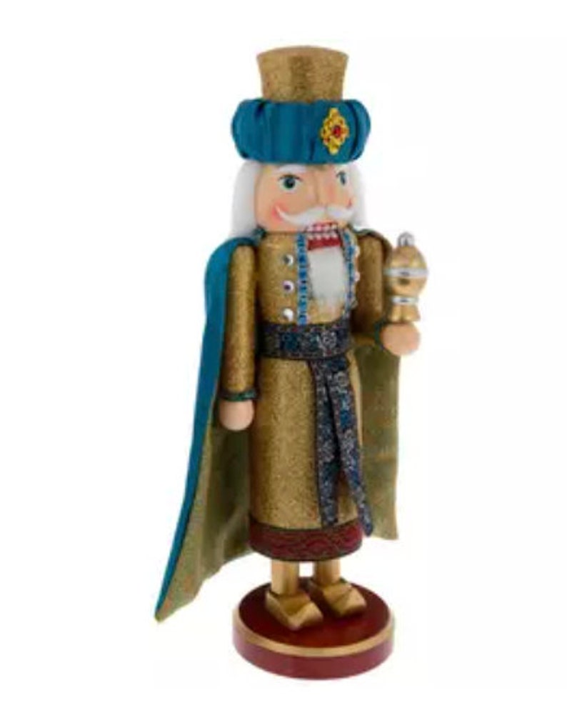May include: A decorative wooden nutcracker figurine. The nutcracker is dressed in a gold and teal outfit with a matching hat. It has a white mustache and holds a golden scepter. The base is a dark red color.