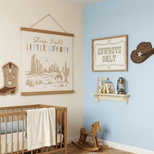 May include: A nursery with a cowboy theme. The room features a crib, a wall hanging with the text "Sleep tight LITTLE COWBOY", a wooden cowboy boot, a sign that says "Cowboys Only", and a wooden cowboy hat.