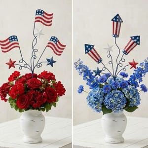 Può includere: Due composizioni floreali in vasi bianchi. Una presenta rose rosse e gerani con accenti di bandiere e stelle in metallo. L'altra ha ortensie blu e delfini con accenti di razzi e stelle in metallo. Entrambe sono patriottiche.