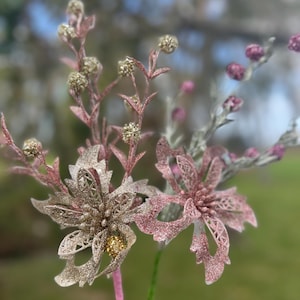 Könnte beinhalten: Ein Strauß aus rosa und goldenen Glitzerblumen mit einem goldenen Glitzermittelpunkt. Die Blumen sitzen auf einem grünen Stiel.